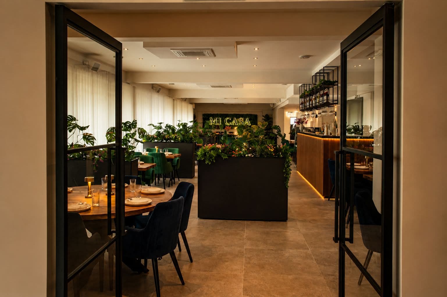 Sfeer bij Mi Casa in Zoetermeer met groene velvet stoelen, plantenwand en neonlogo